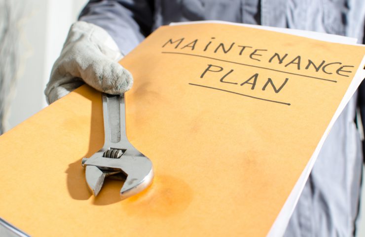 Worker holding a folder of maintenance plan and monkey wrench